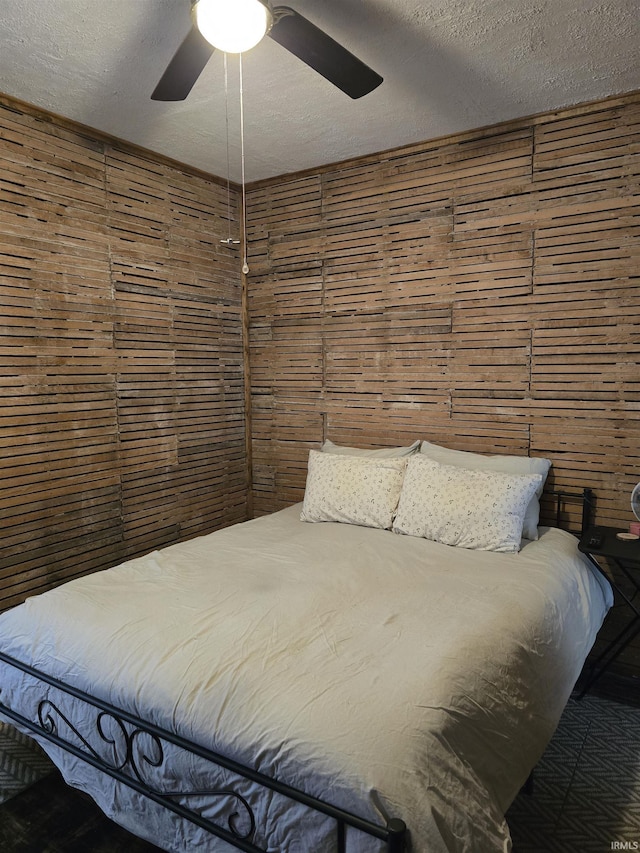 bedroom with ceiling fan, wooden walls, and a textured ceiling