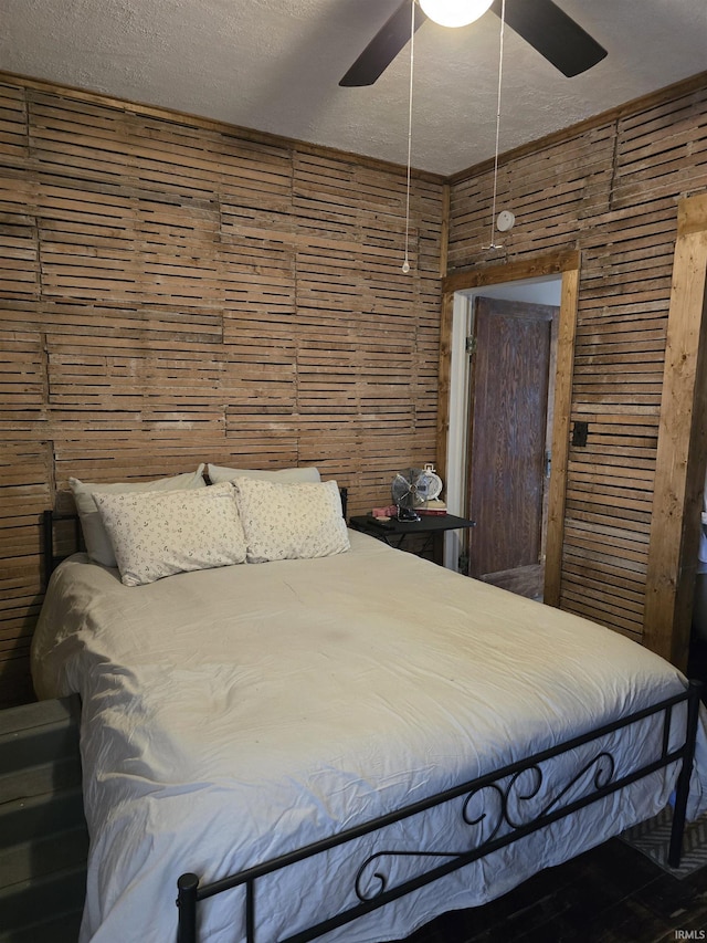 bedroom with ceiling fan, wooden walls, and a textured ceiling