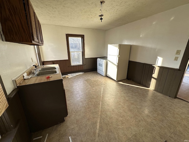 kitchen with sink, wood walls, a textured ceiling, dark brown cabinets, and white appliances