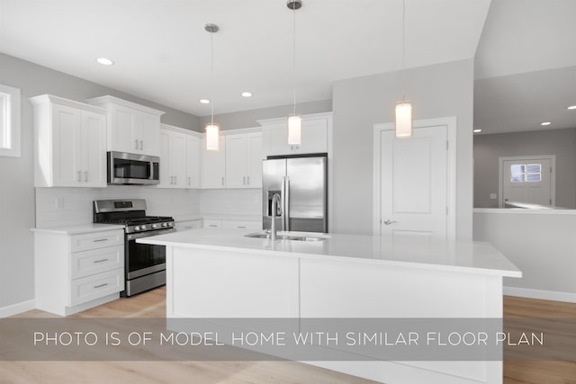 kitchen featuring appliances with stainless steel finishes, pendant lighting, an island with sink, white cabinets, and decorative backsplash