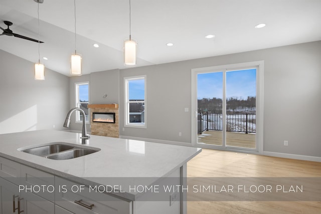 kitchen with sink, a kitchen island with sink, hanging light fixtures, light stone countertops, and light hardwood / wood-style floors