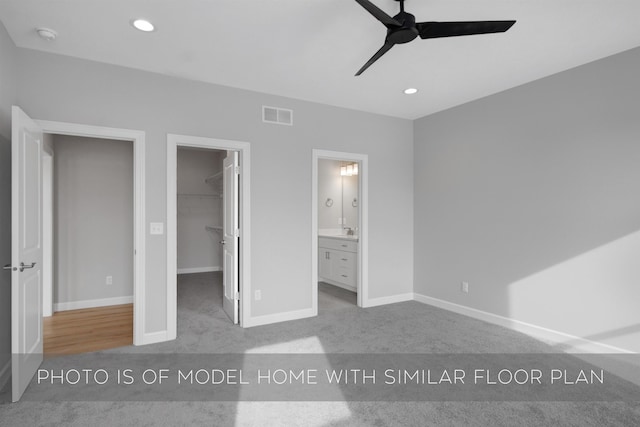 unfurnished bedroom featuring sink, a walk in closet, a closet, ceiling fan, and carpet