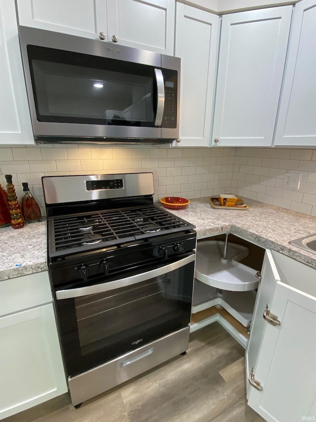 kitchen with light stone counters, light wood-type flooring, stainless steel appliances, decorative backsplash, and white cabinets