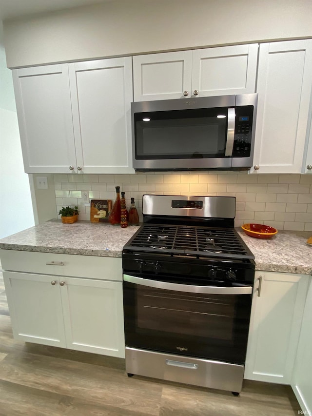 kitchen featuring white cabinetry, decorative backsplash, stainless steel appliances, and light hardwood / wood-style floors