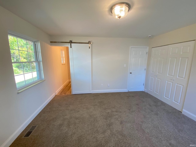 unfurnished bedroom with a barn door, carpet flooring, and a closet