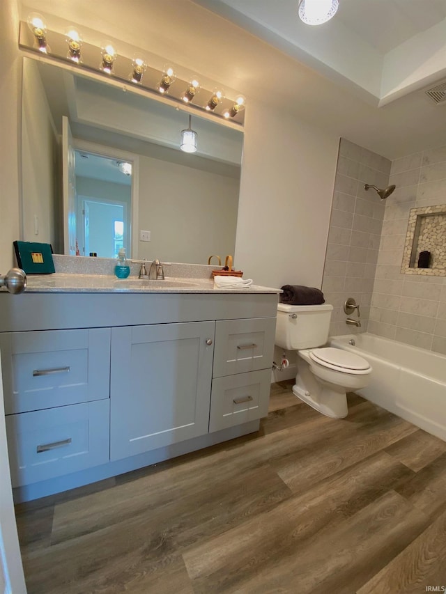 full bathroom with vanity, hardwood / wood-style flooring, toilet, and tiled shower / bath combo