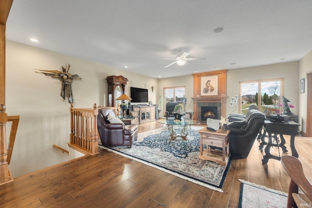 living room featuring wood-type flooring, a large fireplace, ceiling fan, and plenty of natural light