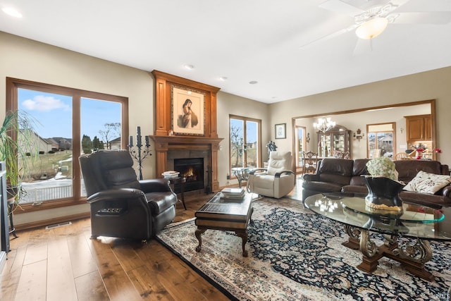 living room with dark hardwood / wood-style flooring, ceiling fan with notable chandelier, and a large fireplace