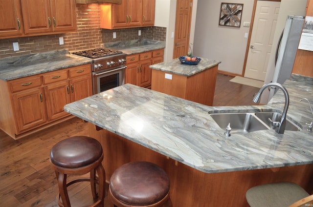 kitchen with an island with sink, light stone countertops, a breakfast bar area, and stainless steel range