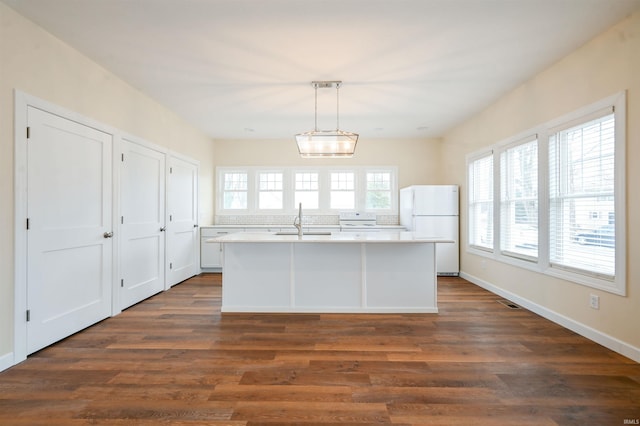 kitchen with dark wood-type flooring, white cabinetry, white refrigerator, a center island with sink, and decorative light fixtures