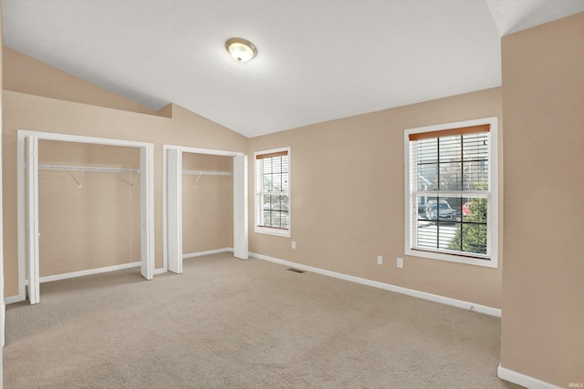 unfurnished bedroom featuring vaulted ceiling, light carpet, and two closets