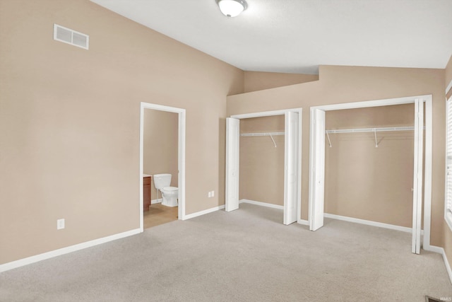 unfurnished bedroom with lofted ceiling, light colored carpet, multiple closets, and ensuite bathroom