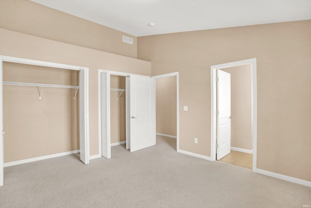 unfurnished bedroom with vaulted ceiling, light carpet, and two closets