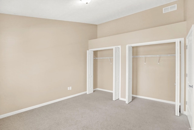 unfurnished bedroom featuring light carpet and two closets