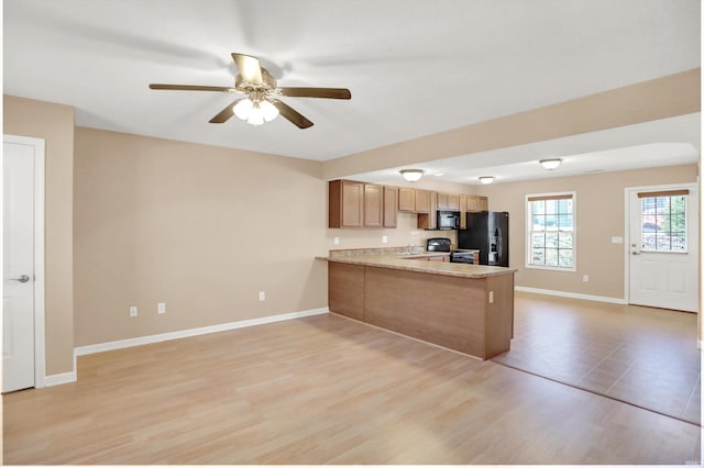 kitchen with kitchen peninsula, ceiling fan, black appliances, light stone counters, and light wood-type flooring