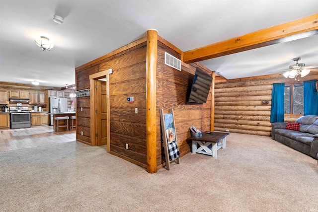 carpeted living room featuring ceiling fan, beamed ceiling, and rustic walls