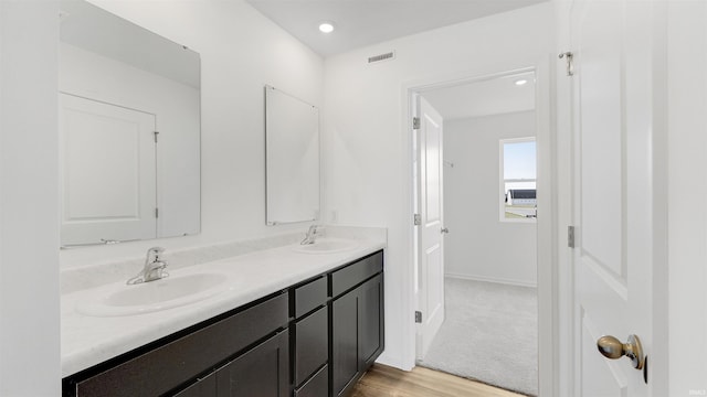 bathroom with visible vents, a sink, double vanity, and wood finished floors