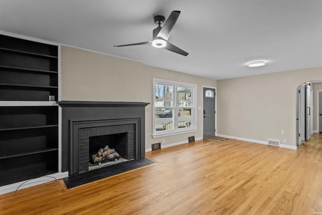 unfurnished living room with ceiling fan, a fireplace, built in features, and light wood-type flooring