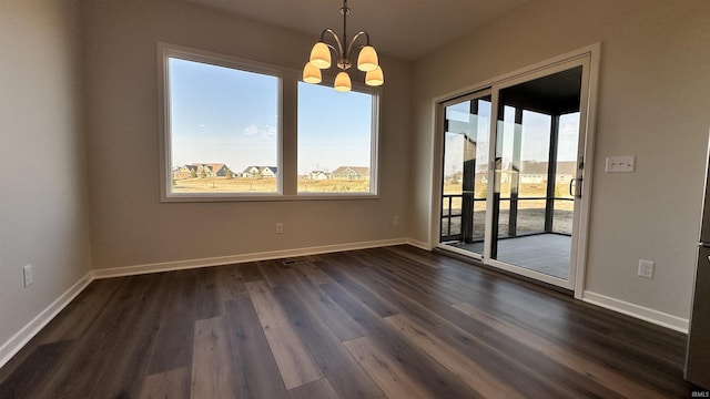 spare room featuring dark wood-style floors, an inviting chandelier, and baseboards