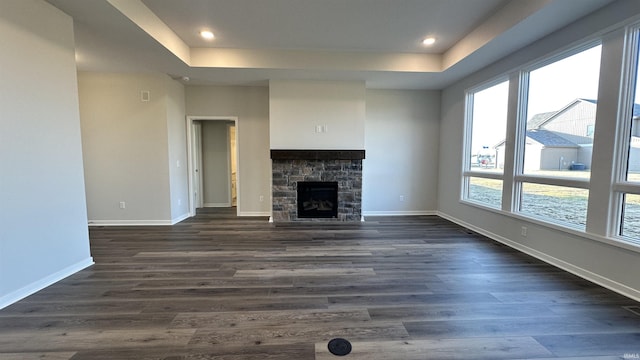 unfurnished living room with a tray ceiling, baseboards, dark wood-style flooring, and a fireplace