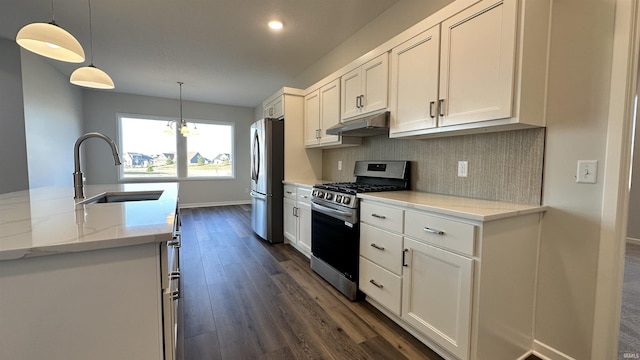 kitchen featuring tasteful backsplash, under cabinet range hood, appliances with stainless steel finishes, dark wood-style floors, and a sink