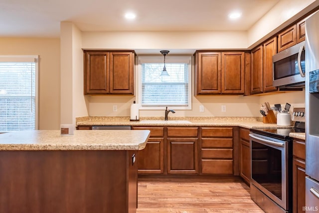 kitchen with appliances with stainless steel finishes, decorative light fixtures, sink, and light wood-type flooring