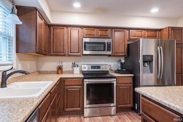 kitchen with sink, decorative light fixtures, light hardwood / wood-style floors, and appliances with stainless steel finishes