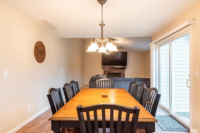 dining room with an inviting chandelier, a brick fireplace, and hardwood / wood-style floors