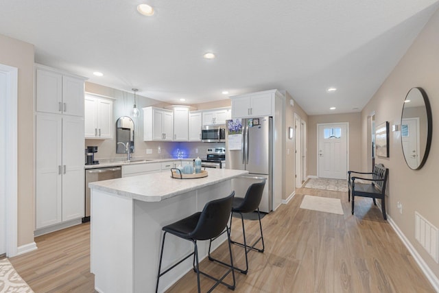 kitchen with sink, stainless steel appliances, a center island, white cabinets, and decorative light fixtures