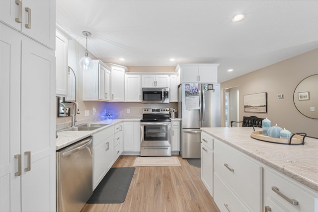 kitchen featuring pendant lighting, sink, white cabinetry, stainless steel appliances, and light hardwood / wood-style floors