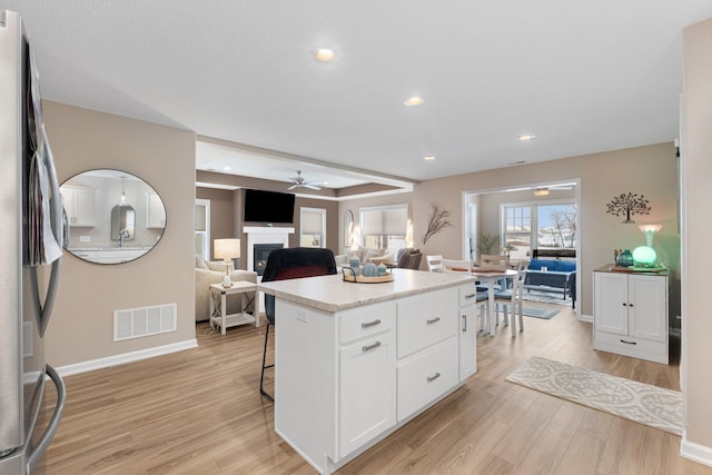 kitchen featuring a kitchen island, stainless steel refrigerator, white cabinetry, a kitchen bar, and light hardwood / wood-style floors