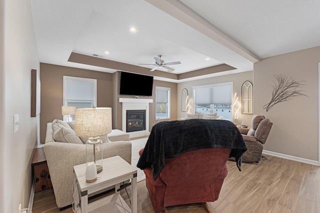 living room with a tray ceiling, light hardwood / wood-style floors, and ceiling fan