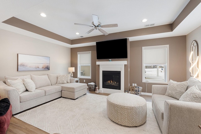 living room with a tray ceiling, ceiling fan, and light wood-type flooring