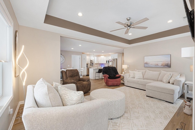 living room featuring ceiling fan, a tray ceiling, and light wood-type flooring