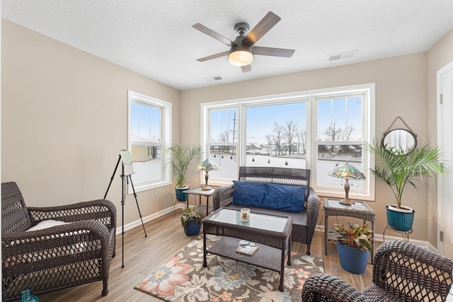 living area with ceiling fan, light hardwood / wood-style floors, and a textured ceiling