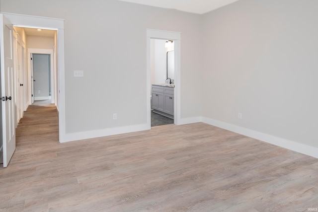 unfurnished bedroom with light wood-type flooring, baseboards, a sink, and ensuite bathroom