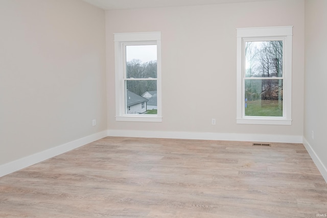 unfurnished room featuring baseboards, plenty of natural light, visible vents, and wood finished floors