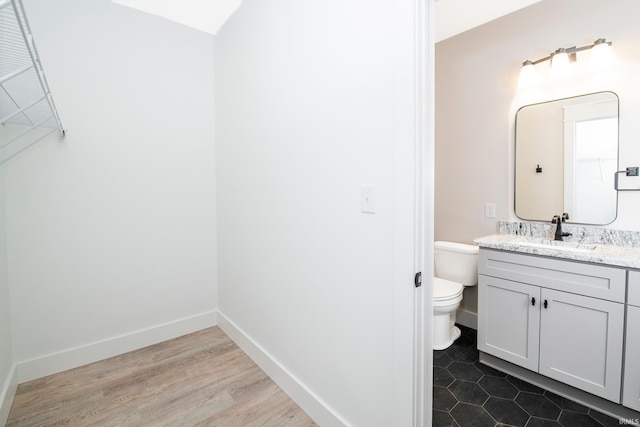 bathroom featuring toilet, baseboards, wood finished floors, and vanity