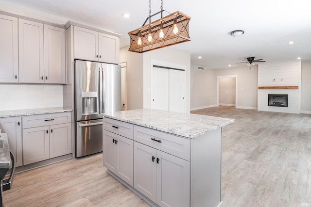 kitchen featuring a large fireplace, ceiling fan, light wood-style flooring, hanging light fixtures, and stainless steel refrigerator with ice dispenser