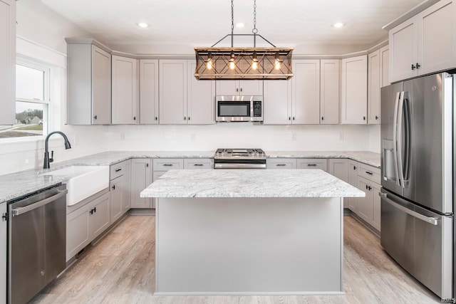 kitchen with stainless steel appliances, light wood-type flooring, a center island, and a sink