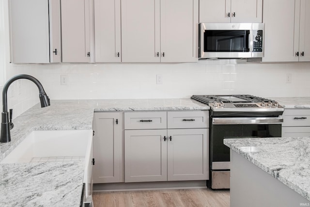 kitchen with tasteful backsplash, light wood-style flooring, appliances with stainless steel finishes, a sink, and light stone countertops