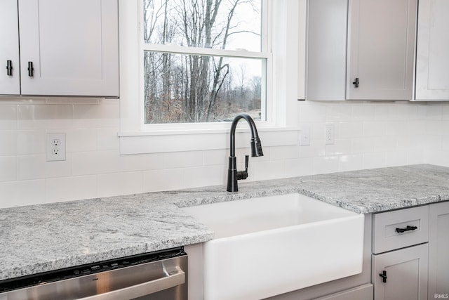 kitchen with a sink, backsplash, stainless steel dishwasher, and light stone countertops