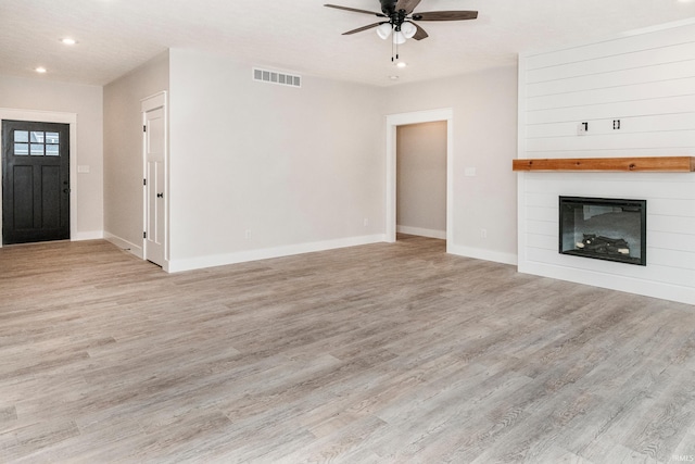 unfurnished living room featuring ceiling fan, a large fireplace, visible vents, baseboards, and light wood-style floors