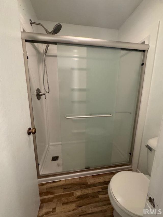 bathroom featuring hardwood / wood-style floors, a shower with shower door, and toilet