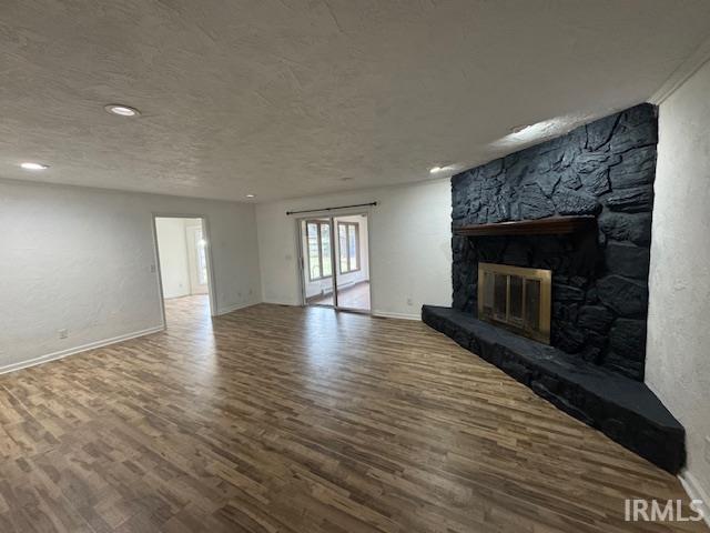 unfurnished living room with hardwood / wood-style floors, a stone fireplace, and a textured ceiling