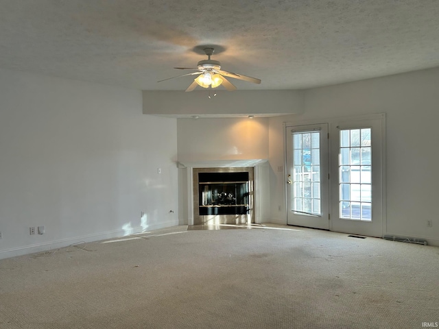 unfurnished living room with ceiling fan, a fireplace, light colored carpet, and a textured ceiling