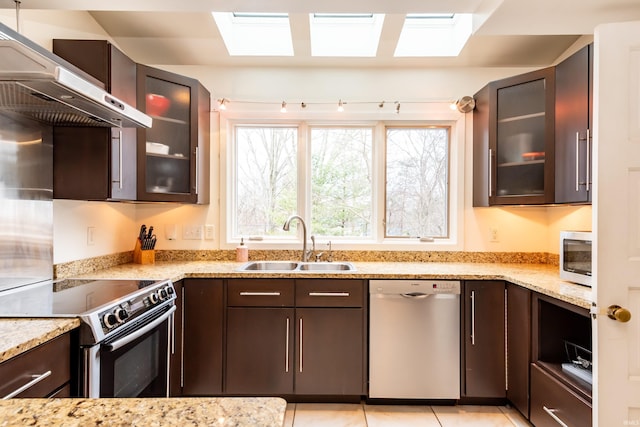 kitchen with stainless steel appliances, light stone countertops, sink, and wall chimney range hood