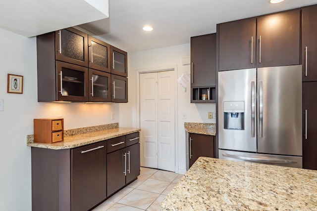 kitchen with light stone counters, dark brown cabinetry, stainless steel fridge, and light tile patterned flooring