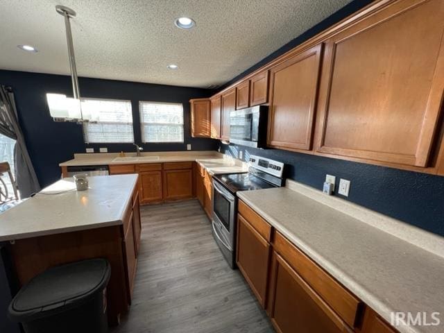 kitchen featuring sink, hanging light fixtures, a textured ceiling, appliances with stainless steel finishes, and hardwood / wood-style floors