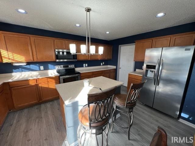 kitchen featuring a kitchen island, hardwood / wood-style floors, pendant lighting, stainless steel appliances, and a textured ceiling